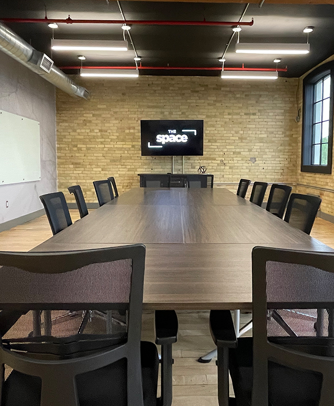 a view of the long, board room table with a tv on the brick wall